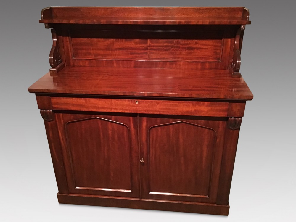 An antique flame mahogany side cabinet featuring an upper shelf supported by scrolled brackets above two panelled cupboard doors.