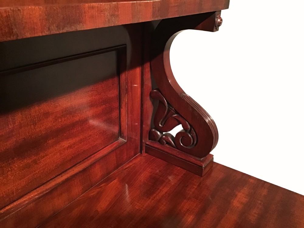 An antique flame mahogany side cabinet featuring an upper shelf supported by scrolled brackets above two panelled cupboard doors. View IV