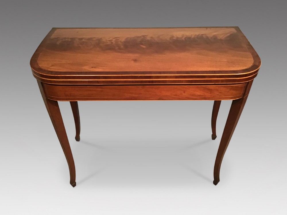 An antique mahogany fold-over tea table with crossbanded top inlay and slender curved legs set against a plain grey background.