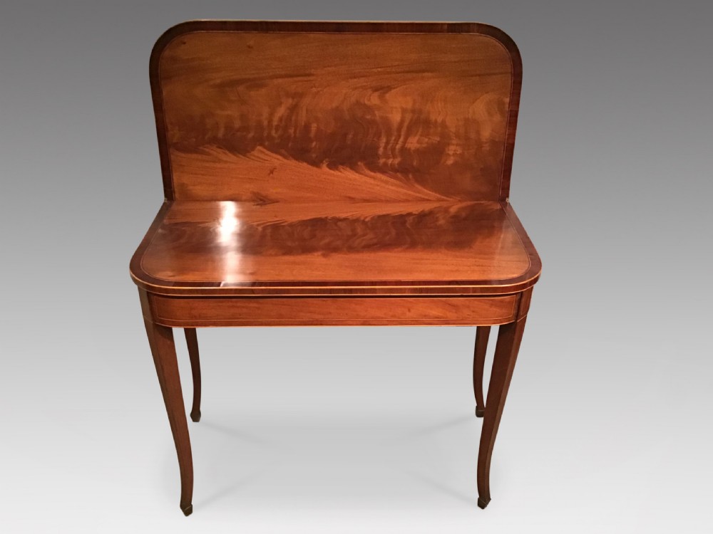 An antique mahogany fold-over tea table with crossbanded top inlay and slender curved legs set against a plain grey background. View III