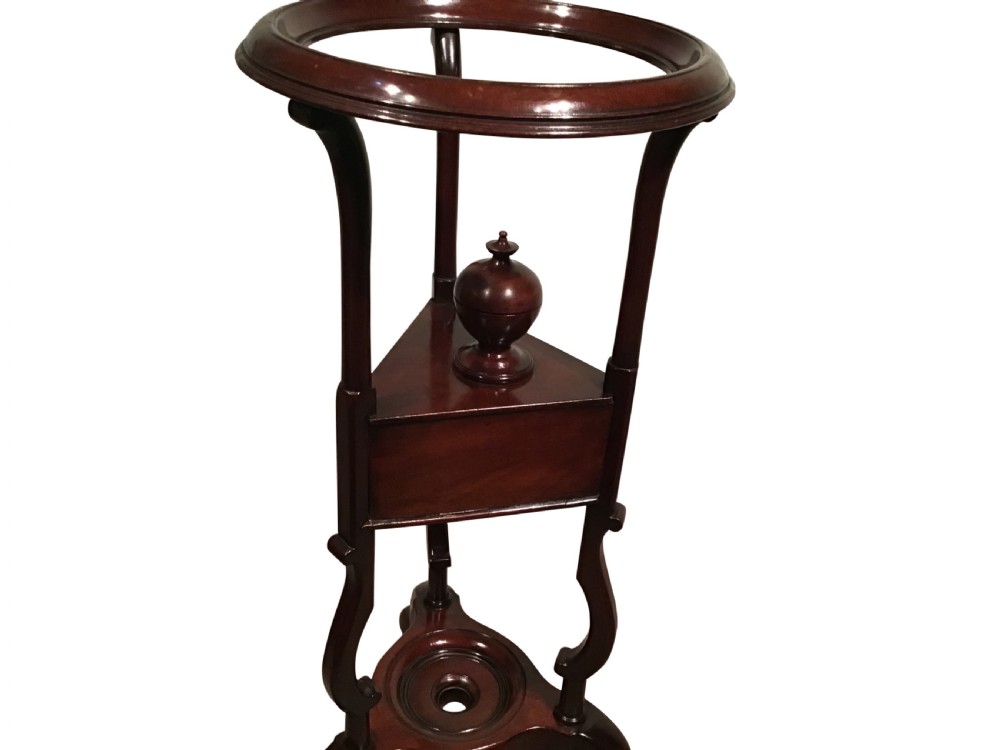 A dark mahogany Georgian wig stand featuring a circular top ring, a triangular drawer section with an urn finial, and a tripod base with cabriole legs. View II