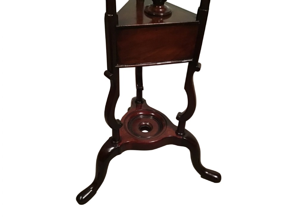A dark mahogany Georgian wig stand featuring a circular top ring, a triangular drawer section with an urn finial, and a tripod base with cabriole legs. View V