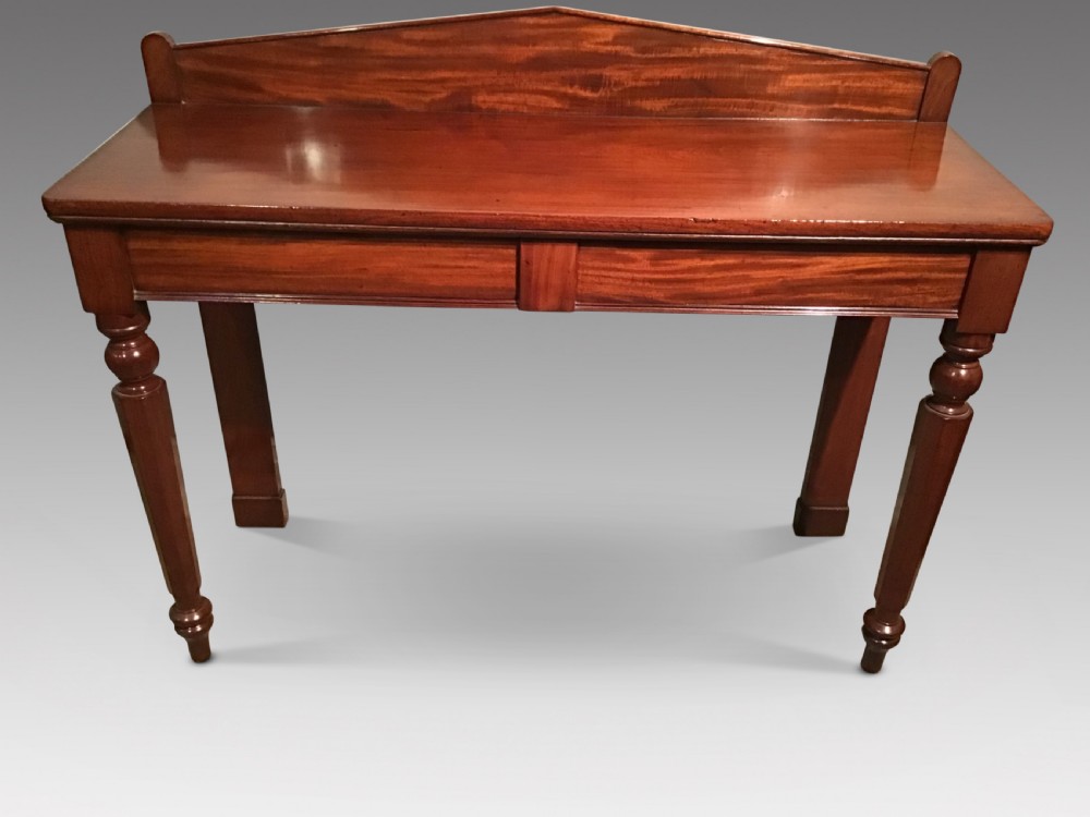 A mahogany serving table featuring a raised shaped backboard gallery, polished rectangular top, plain apron, and turned front legs.