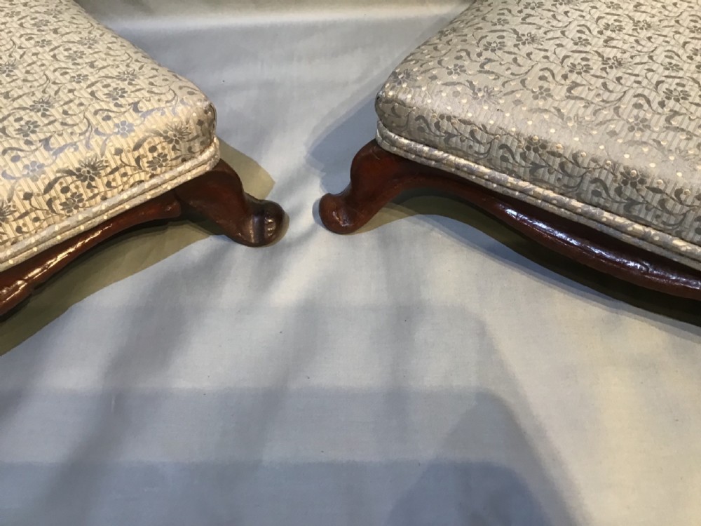 A pair of low antique footstools featuring dark carved mahogany cabriole legs and silver floral patterned upholstery. View II