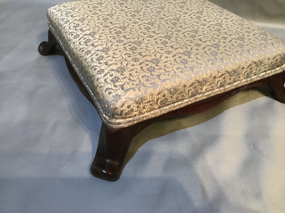 A pair of low antique footstools featuring dark carved mahogany cabriole legs and silver floral patterned upholstery. View IV