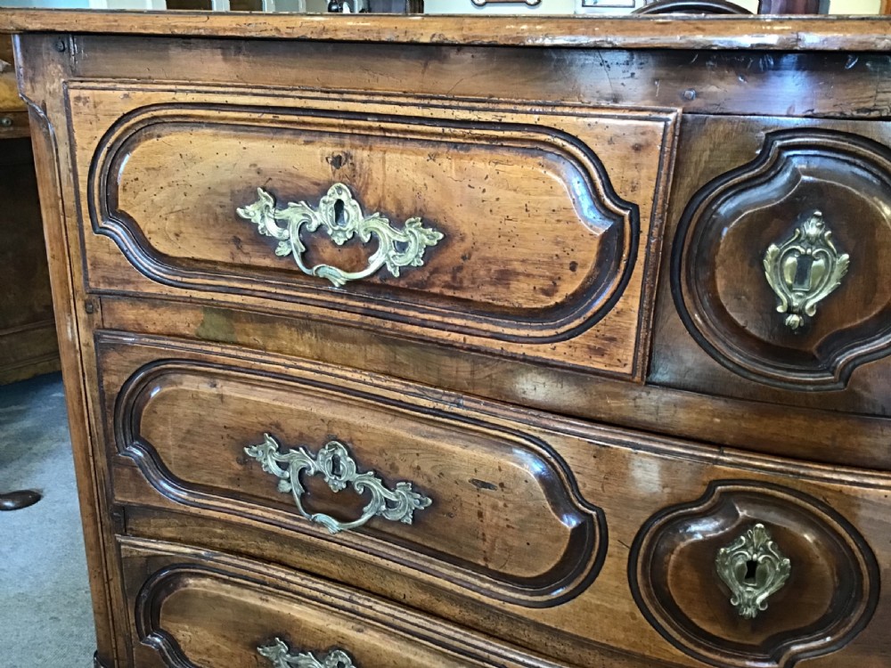 An antique French Louis XV style walnut commode featuring three contoured drawers with moulded panels and ornamental brass handles on cabriole legs. View V