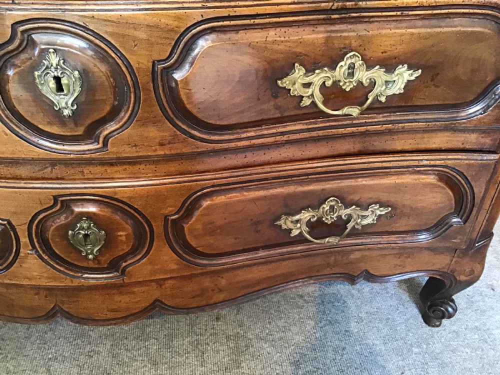 An antique French Louis XV style walnut commode featuring three contoured drawers with moulded panels and ornamental brass handles on cabriole legs. View VI