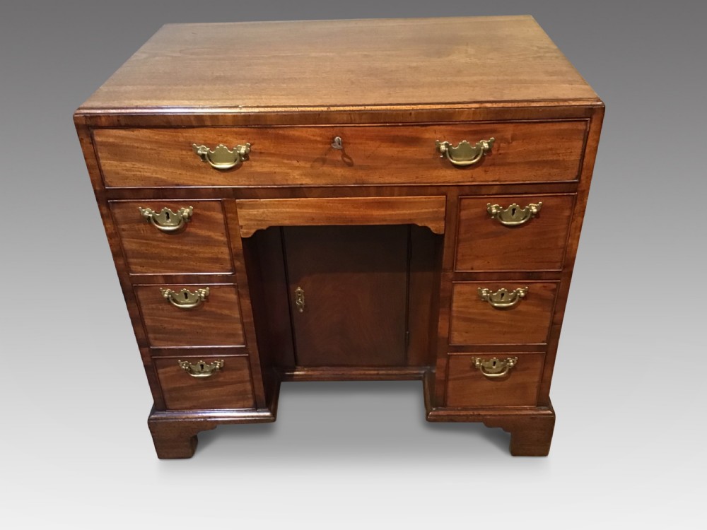 An antique Georgian mahogany kneehole desk featuring a long top drawer, six side drawers, a central recessed cupboard, and brass handles resting on bracket feet.