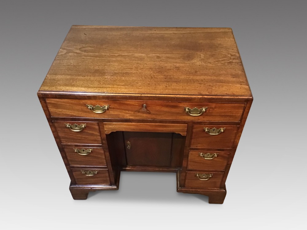 An antique Georgian mahogany kneehole desk featuring a long top drawer, six side drawers, a central recessed cupboard, and brass handles resting on bracket feet. View II