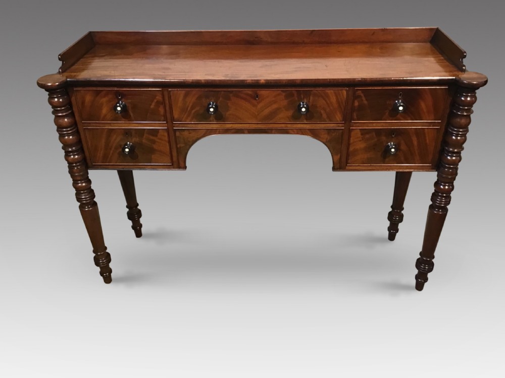 An antique mahogany hall table featuring a gallery back, five drawers with turned knobs, an arched kneehole centre, and four turned legs.