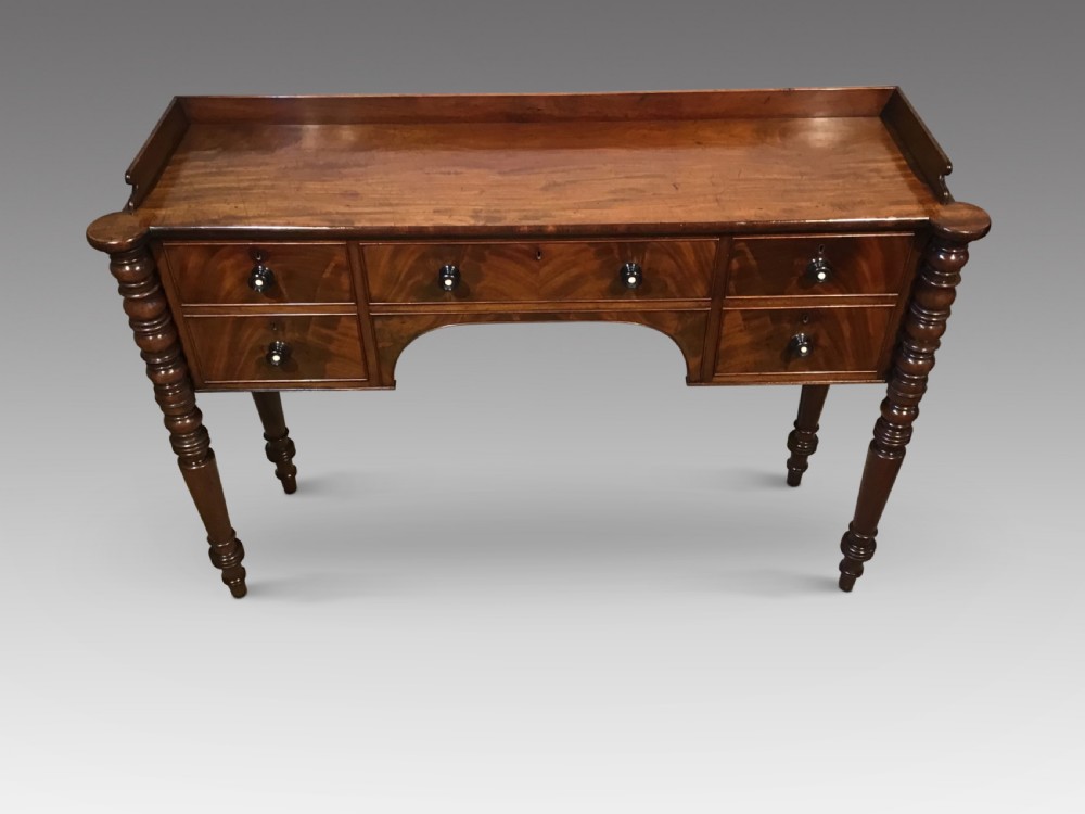 An antique mahogany hall table featuring a gallery back, five drawers with turned knobs, an arched kneehole centre, and four turned legs. View II