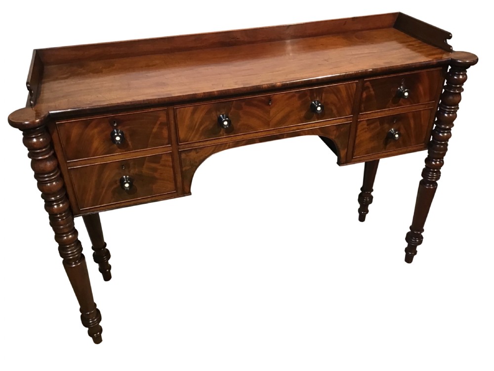 An antique mahogany hall table featuring a gallery back, five drawers with turned knobs, an arched kneehole centre, and four turned legs. View III