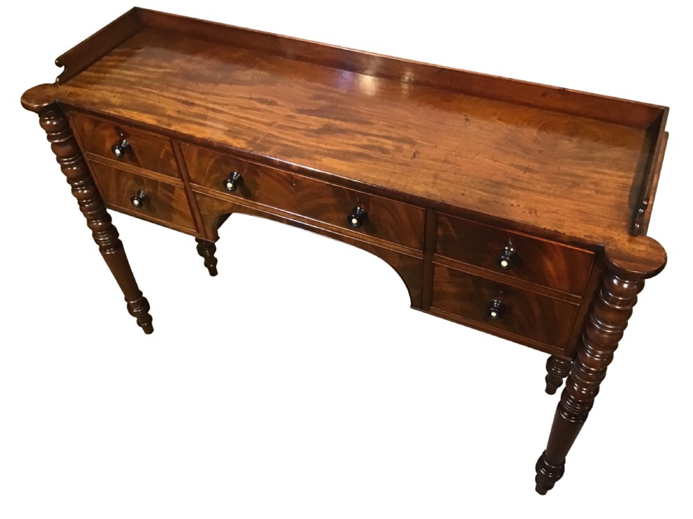 An antique mahogany hall table featuring a gallery back, five drawers with turned knobs, an arched kneehole centre, and four turned legs. View IV