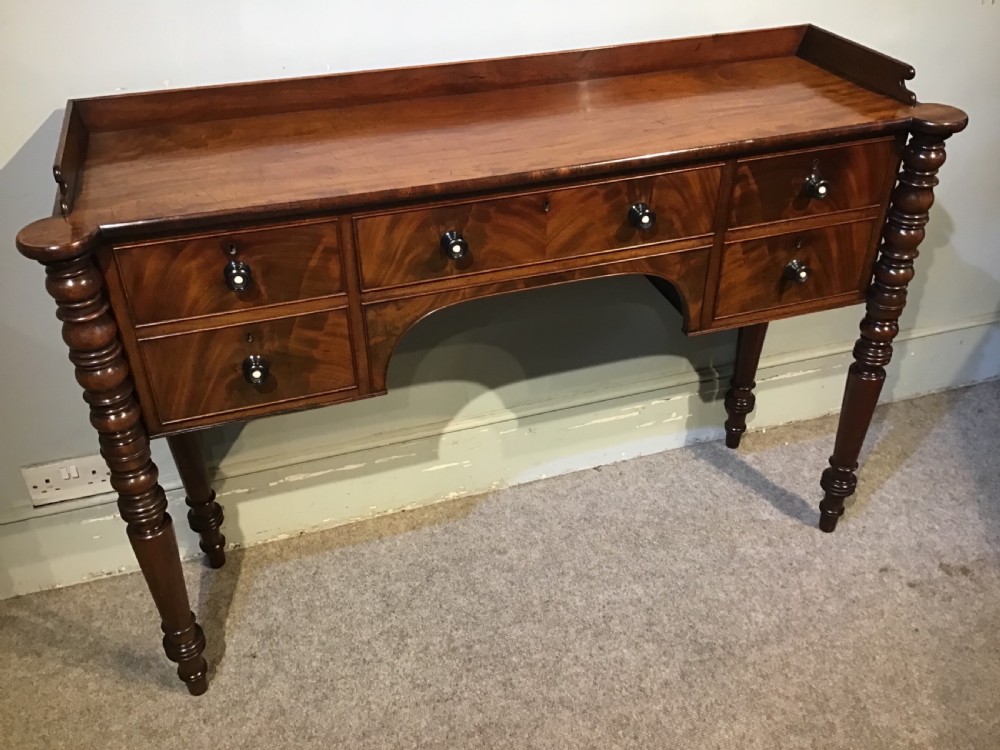 An antique mahogany hall table featuring a gallery back, five drawers with turned knobs, an arched kneehole centre, and four turned legs. View VI