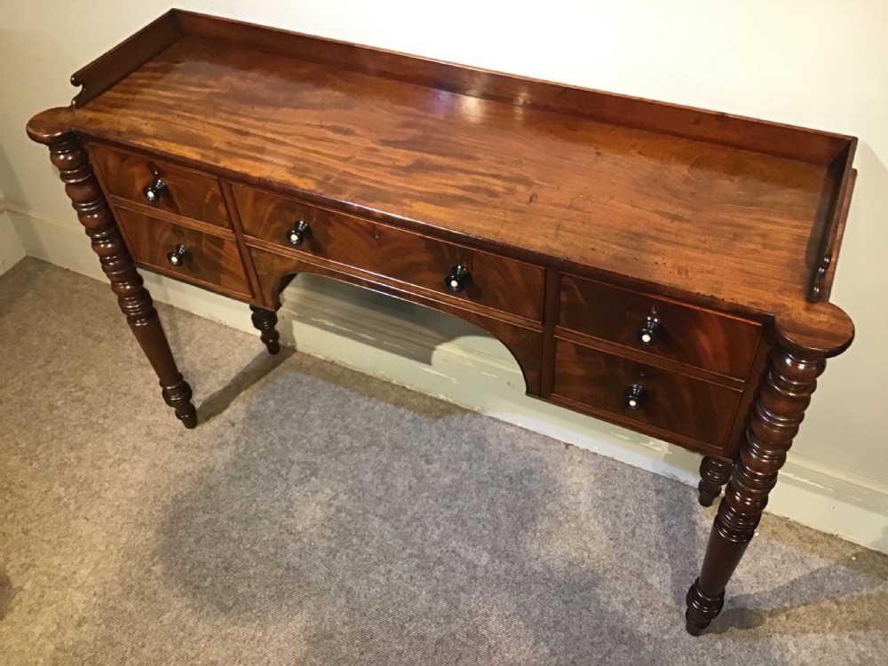 An antique mahogany hall table featuring a gallery back, five drawers with turned knobs, an arched kneehole centre, and four turned legs. View VII