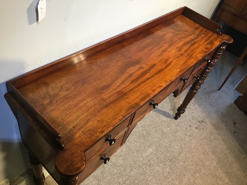 An antique mahogany hall table featuring a gallery back, five drawers with turned knobs, an arched kneehole centre, and four turned legs. View VIII
