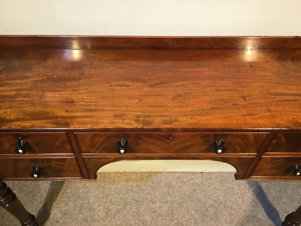An antique mahogany hall table featuring a gallery back, five drawers with turned knobs, an arched kneehole centre, and four turned legs. View IX