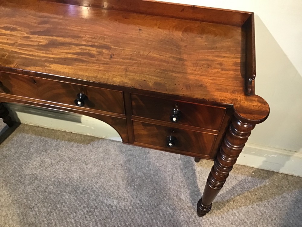 An antique mahogany hall table featuring a gallery back, five drawers with turned knobs, an arched kneehole centre, and four turned legs. View X