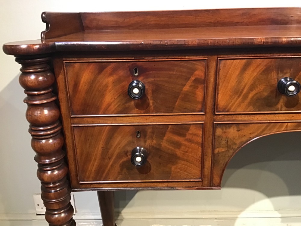 An antique mahogany hall table featuring a gallery back, five drawers with turned knobs, an arched kneehole centre, and four turned legs. View XI