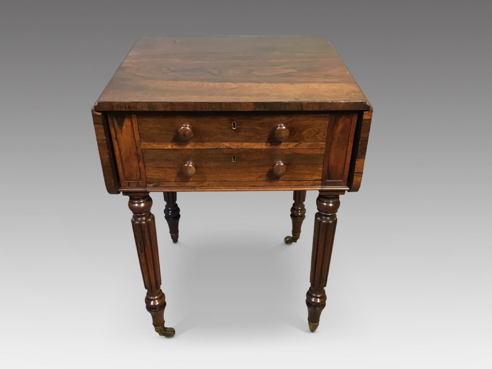 An antique mahogany Pembroke work table with two drawers, turned wooden knobs, drop-leaf sides, reeded legs, and brass castors.