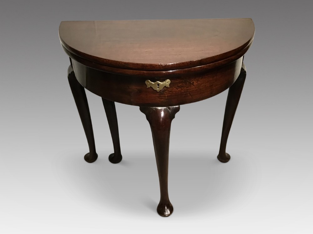 A dark mahogany demi-lune fold-over tea table featuring cabriole legs ending in pad feet and a central brass keyhole escutcheon.