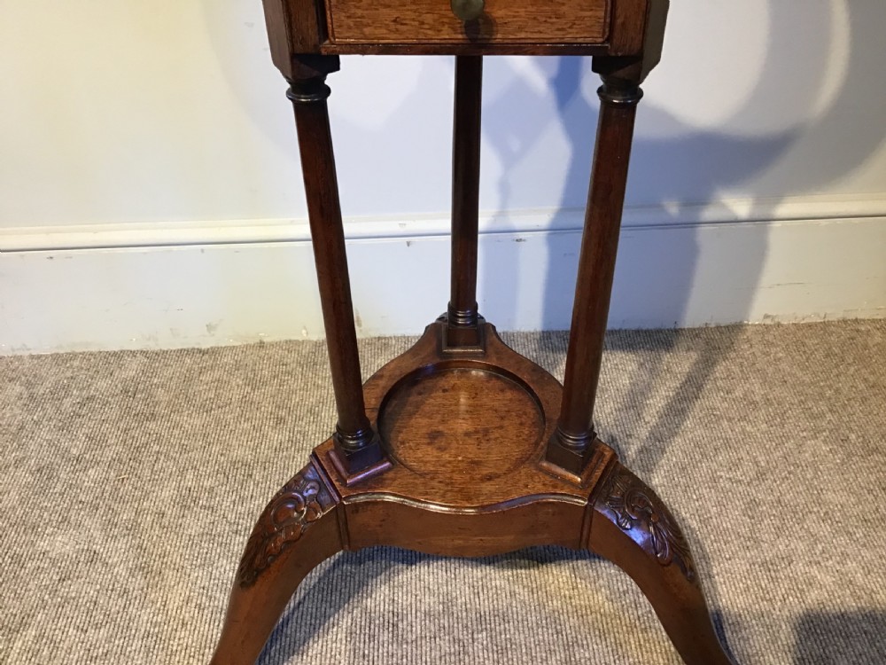 An antique Georgian mahogany tripod washstand featuring an upper basin ring, a middle triangular drawer section with an urn finial, and cabriole legs. View V