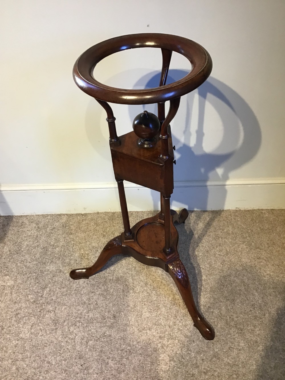 An antique Georgian mahogany tripod washstand featuring an upper basin ring, a middle triangular drawer section with an urn finial, and cabriole legs. View VII