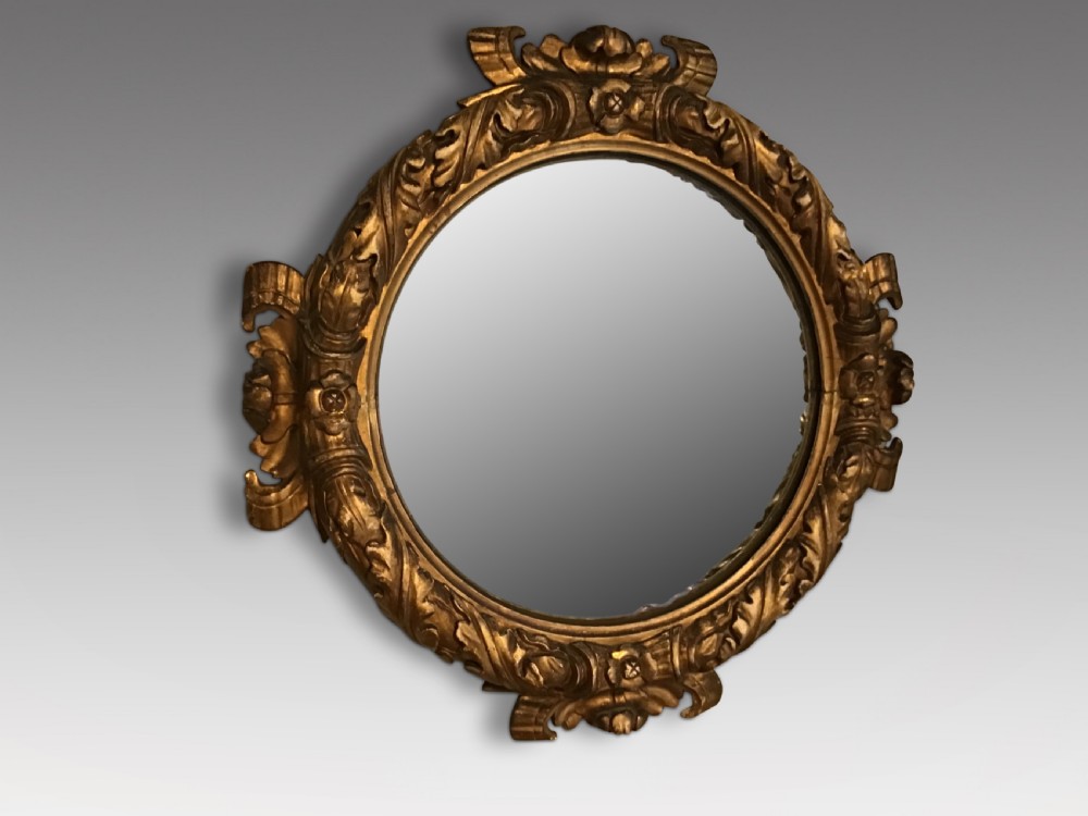A circular convex wall mirror set within a carved gold-gilded frame embellished with acanthus leaf motifs.