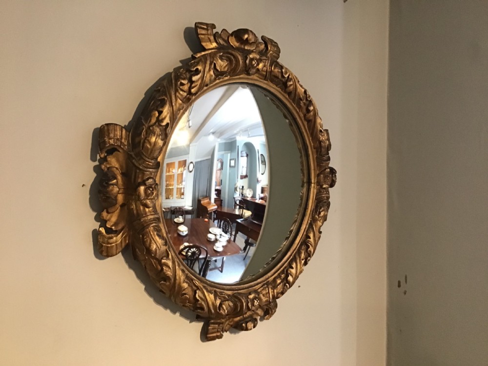 A circular convex wall mirror set within a carved gold-gilded frame embellished with acanthus leaf motifs. View II