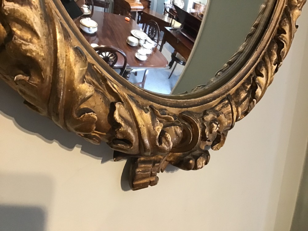 A circular convex wall mirror set within a carved gold-gilded frame embellished with acanthus leaf motifs. View III