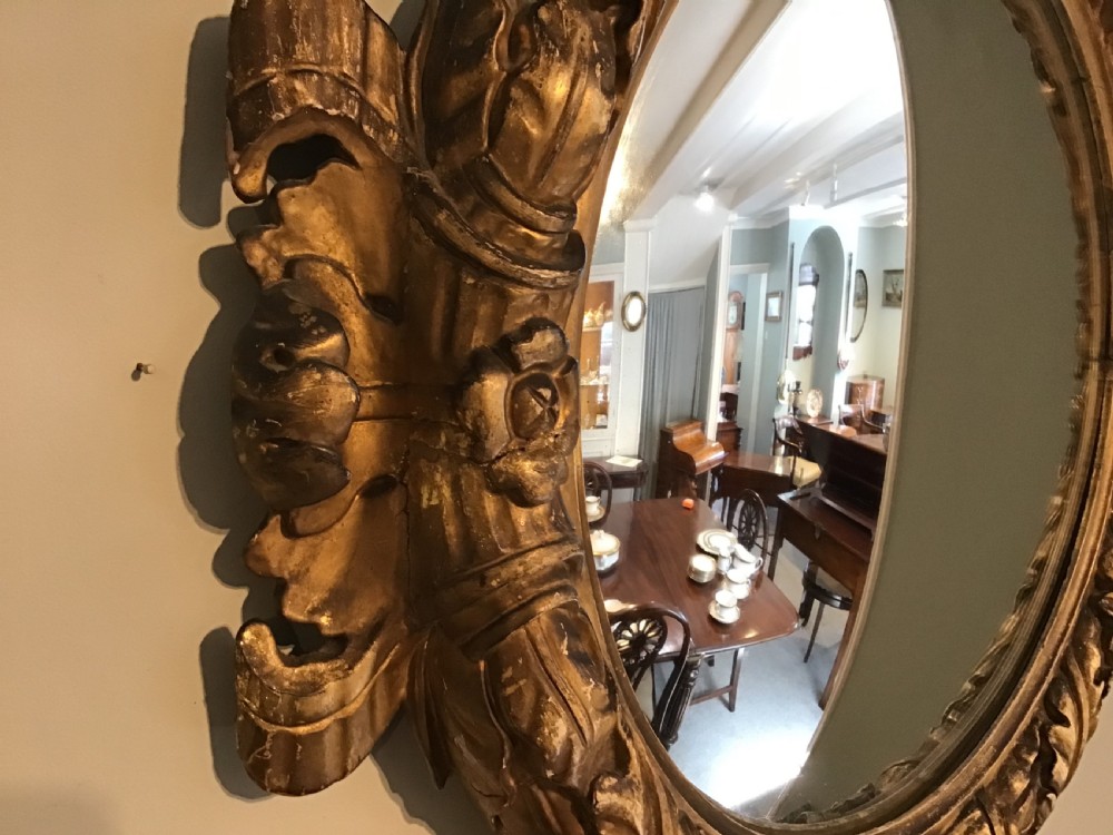 A circular convex wall mirror set within a carved gold-gilded frame embellished with acanthus leaf motifs. View IV