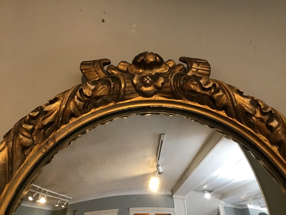 A circular convex wall mirror set within a carved gold-gilded frame embellished with acanthus leaf motifs. View V