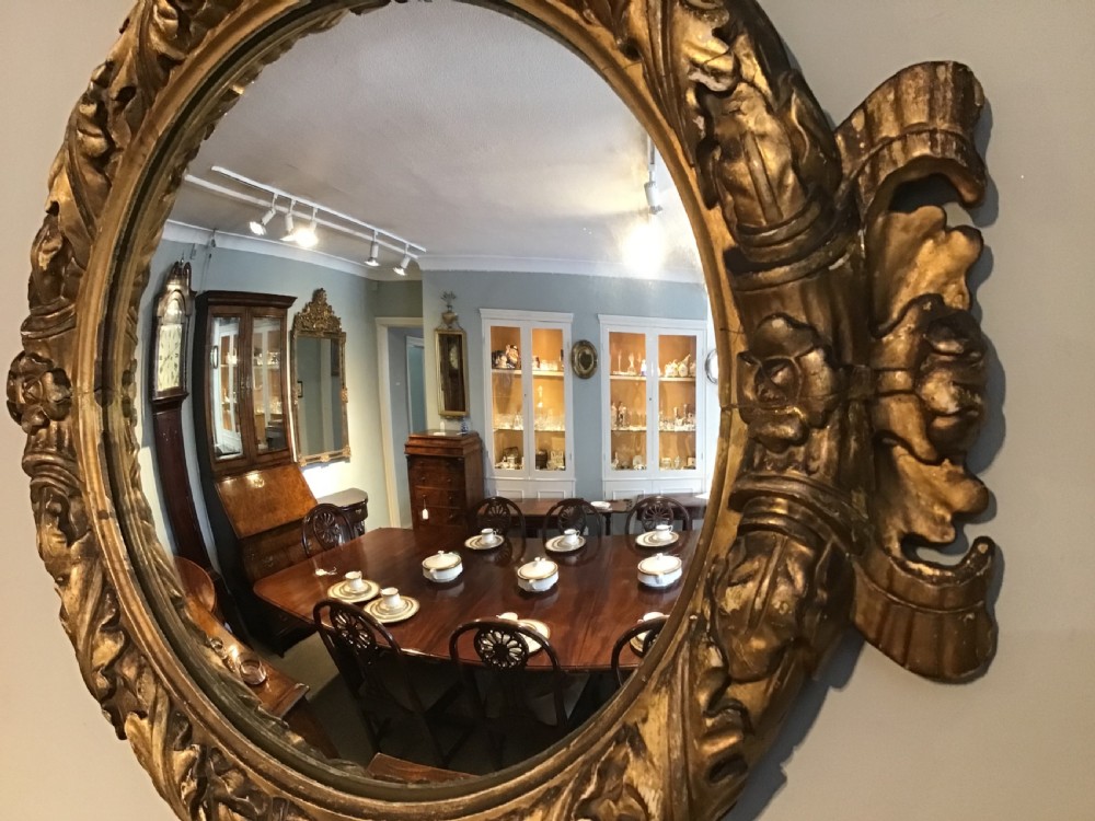 A circular convex wall mirror set within a carved gold-gilded frame embellished with acanthus leaf motifs. View VI