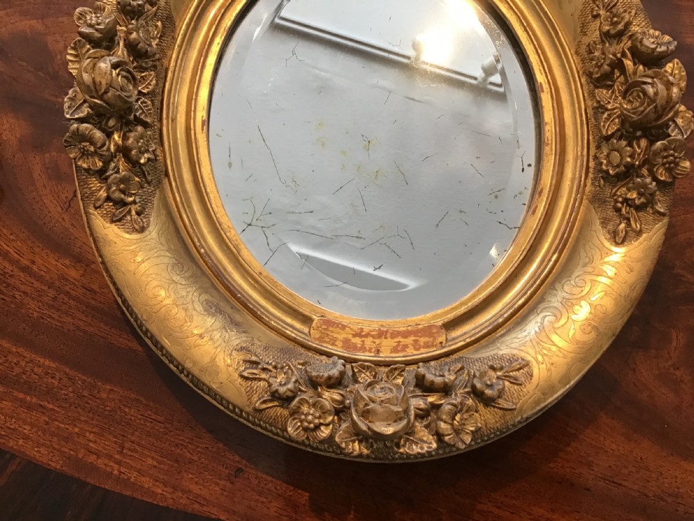 A pair of oval giltwood mirrors featuring detailed floral moulding and engraved detailing along the gilded frames. View II
