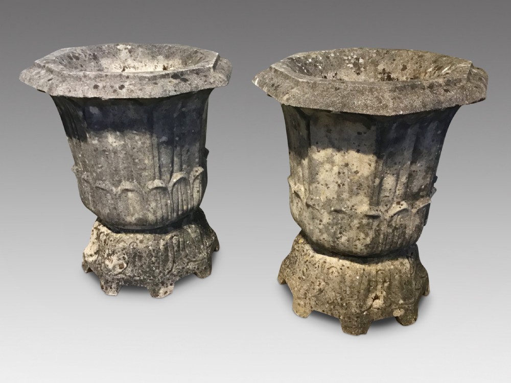 A pair of weathered grey cast stone garden urns with fluted rims and decorative pedestals displaying natural moss and lichen growth.