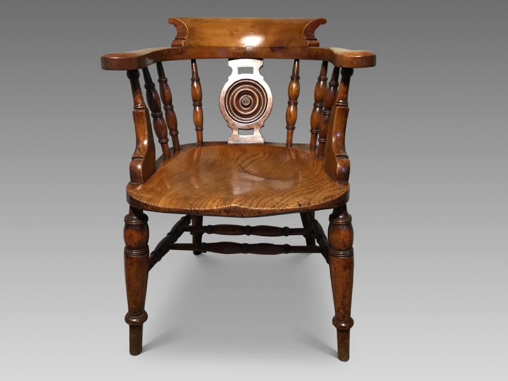 An antique wooden smokers bow armchair with turned spindles, a carved central splat, and a shaped saddle seat. View II