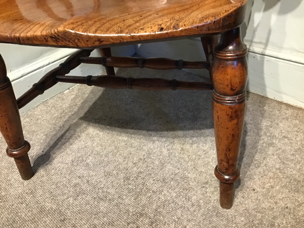 An antique wooden smokers bow armchair with turned spindles, a carved central splat, and a shaped saddle seat. View III
