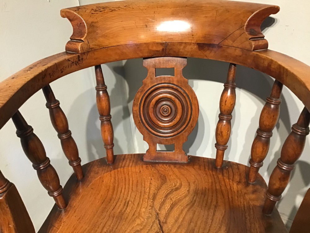 An antique wooden smokers bow armchair with turned spindles, a carved central splat, and a shaped saddle seat. View V