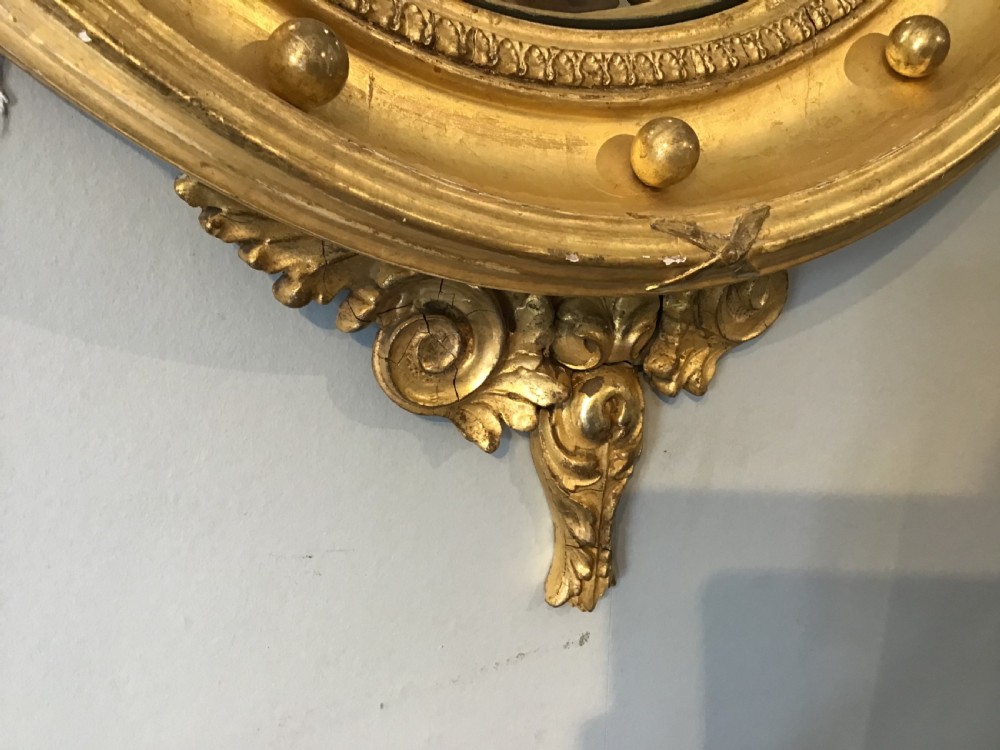 A circular Regency giltwood convex mirror featuring a carved eagle cresting at the top, decorative spheres around the frame rim, and an acanthus leaf pendant below. View III