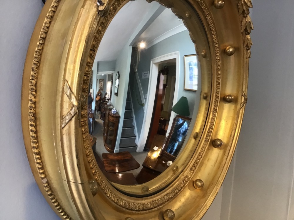 A circular Regency giltwood convex mirror featuring a carved eagle cresting at the top, decorative spheres around the frame rim, and an acanthus leaf pendant below. View IV