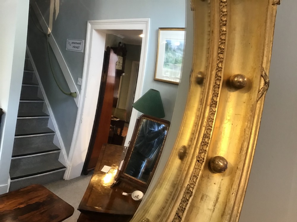 A circular Regency giltwood convex mirror featuring a carved eagle cresting at the top, decorative spheres around the frame rim, and an acanthus leaf pendant below. View V