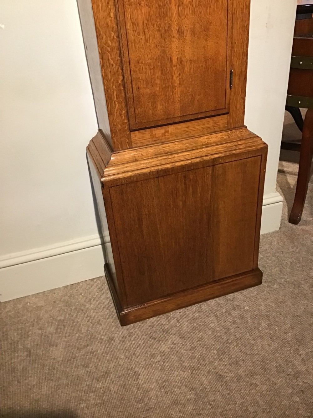 An antique oak longcase clock featuring a painted dial with Roman numerals, a swan-neck pediment with a brass finial, and a wooden trunk with an arched door. View VI