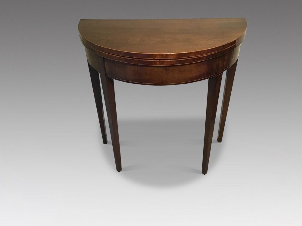 A semi-circular antique mahogany demi-lune card table with a fold-over top supported by four tapered square legs.