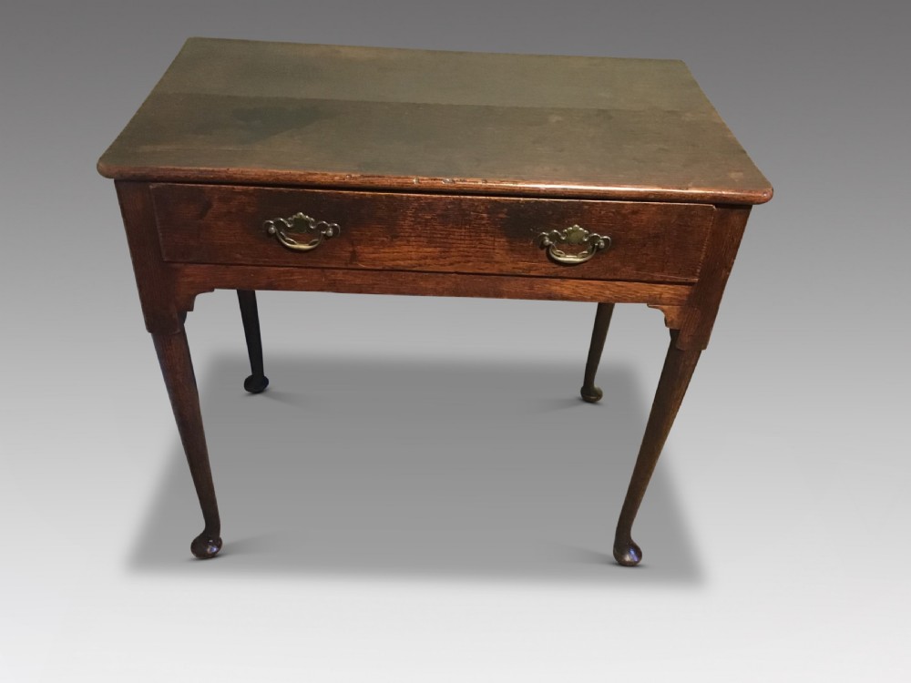 An antique oak side table featuring a single drawer with brass swan-neck handles and cabriole legs resting on pad feet.