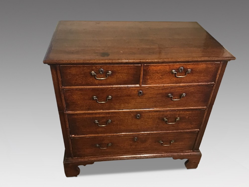 A Georgian oak chest of drawers displaying a two short over three long drawer arrangement with brass swan-neck handles and bracket feet. View II
