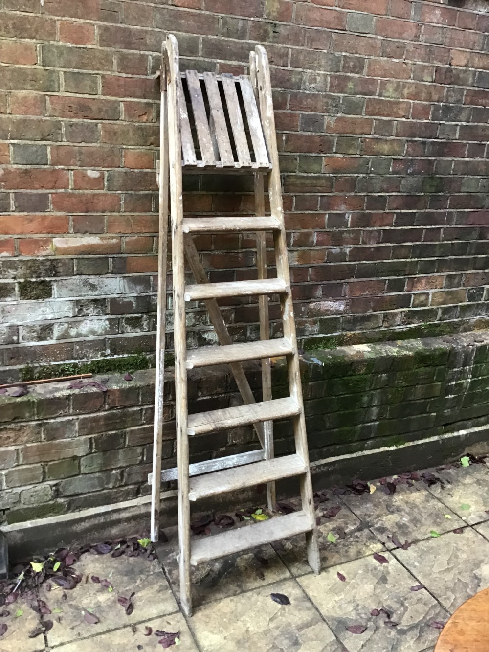 A tall weathered wooden A-frame stepladder featuring a slatted top platform and multiple flat treads.