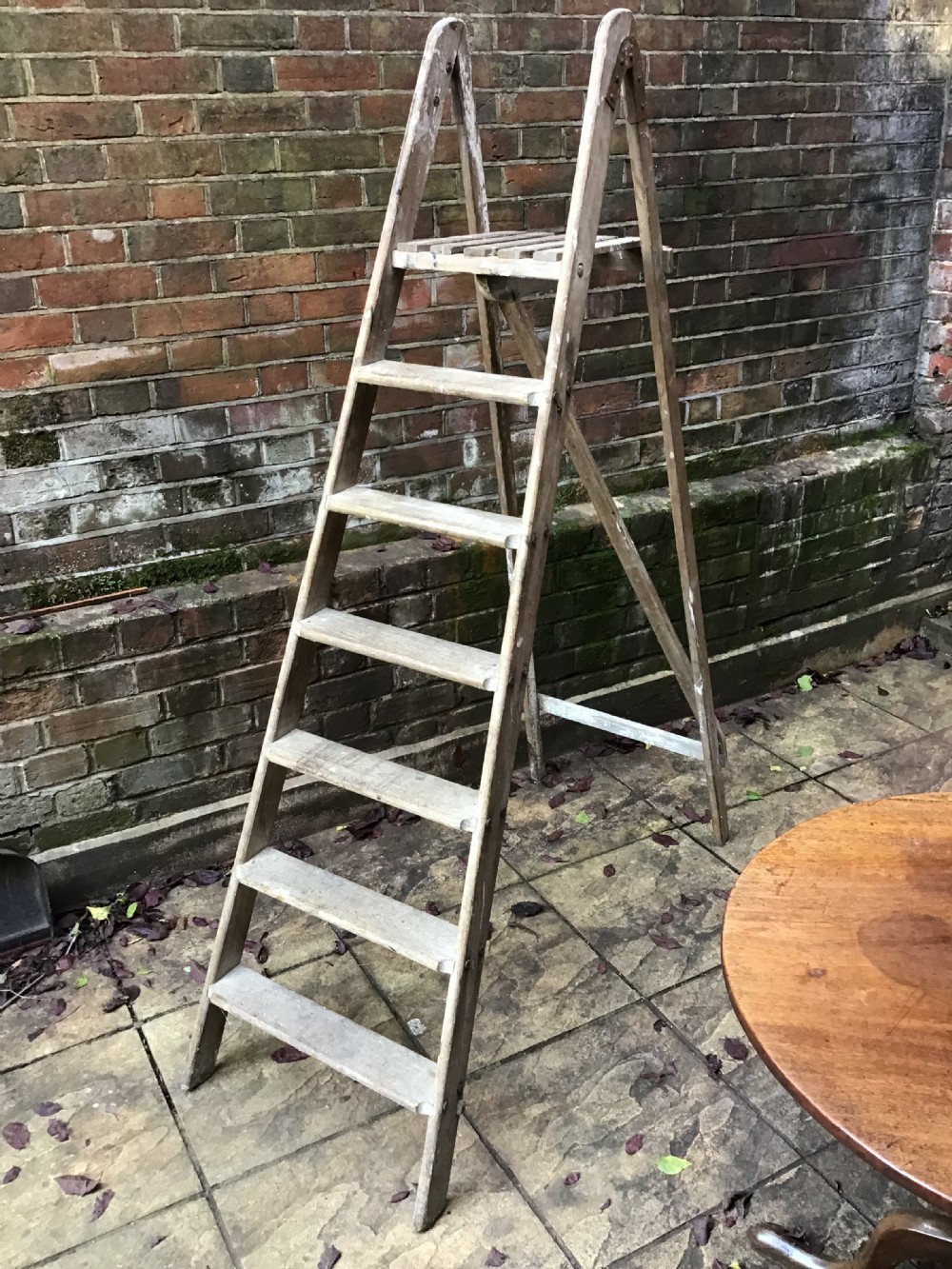 A tall weathered wooden A-frame stepladder featuring a slatted top platform and multiple flat treads. View II