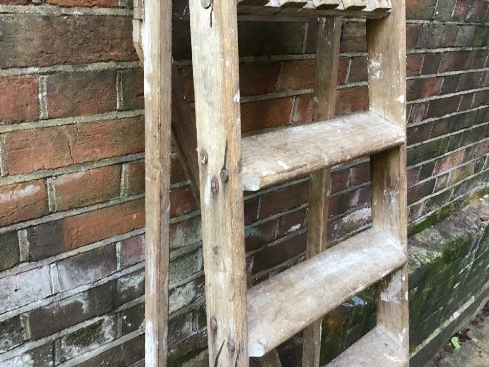 A tall weathered wooden A-frame stepladder featuring a slatted top platform and multiple flat treads. View III