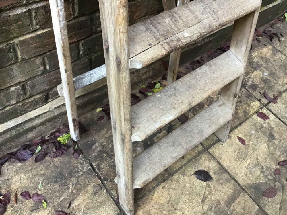 A tall weathered wooden A-frame stepladder featuring a slatted top platform and multiple flat treads. View V