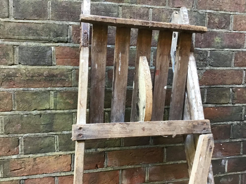 A tall weathered wooden A-frame stepladder featuring a slatted top platform and multiple flat treads. View X